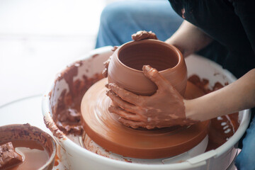 Female hands throwing a large sized bowl on a potter's wheel in a sunlit pottery studio