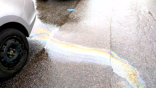 gasoline is leaking out of the car onto the asphalt. rainbow streaks of spilled gasoline on wet asphalt.