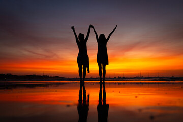 Silhouette of Two friends celebrating sunset on the beach
