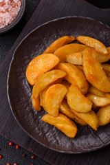 Baked potato wedges with cheese and herbs on a dark background