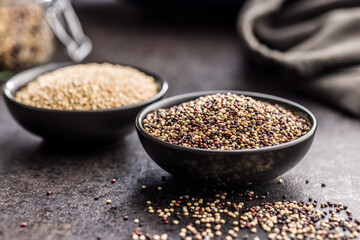 Mixed uncooked quinoa seeds in bowl on black table.
