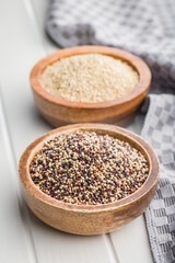 Mixed uncooked quinoa seeds in bowl on white table.