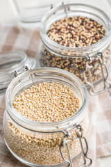 Mixed uncooked quinoa seeds in jar on checkered napkin