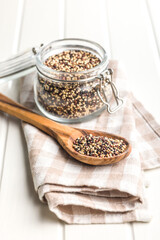 Mixed uncooked quinoa seeds on wooden spoon on white table.