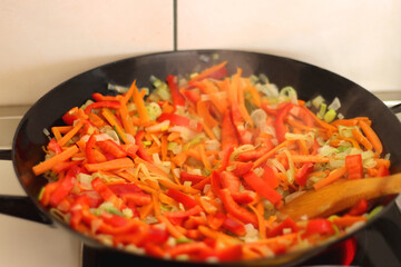 Stir frying chopped leek, carrots and red bell peppers in a wok. Selective focus.