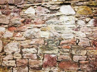 Background: Uneven old wall with different colored patched clinker bricks. Closeup. Walls of Edinburgh, Scotland, UK. Sandstone. Moss stains. Antique