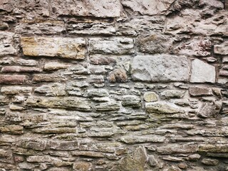 Background: Uneven old wall with different colored patched clinker bricks. Closeup. Walls of Edinburgh, Scotland, UK. Sandstone. Moss stains. Antique