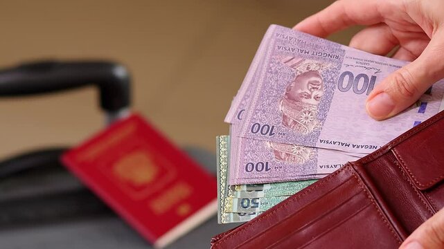 Close up of a female traveler hands counting money while packing a suitcase for a holiday trip. Preparing money and luggage for travel. Close up of a woman hands counting Malaysian ringgit cash money.
