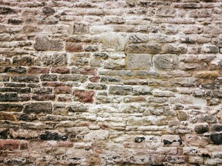 Background: Uneven old wall with different colored patched clinker bricks. Closeup. Walls of Edinburgh, Scotland, UK. Sandstone. Moss stains. Antique