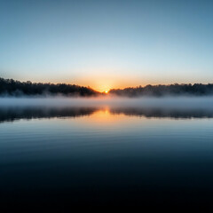 Fototapeta premium Misty sunrise over calm lake waters in early morning
