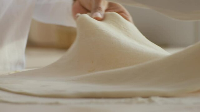 A woman expertly rolls out dough on a floured surface in a bright, inviting kitchen. Her passion for baking is evident as she carefully prepares her next culinary creation.