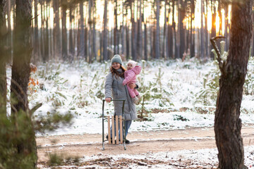 Mother walking in snowy forest with daughter in pink snowsuit and sled