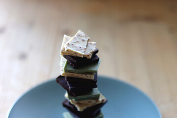 Pile of various chocolate pieces on a plate. Dark, white and matcha chocolate. Selective focus.