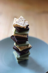 Pile of various chocolate pieces on a plate. Dark, white and matcha chocolate. Selective focus.