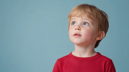 Naklejka premium Young Boy Gazing Upward with Curiosity Against a Blue Background in Bright Natural Light