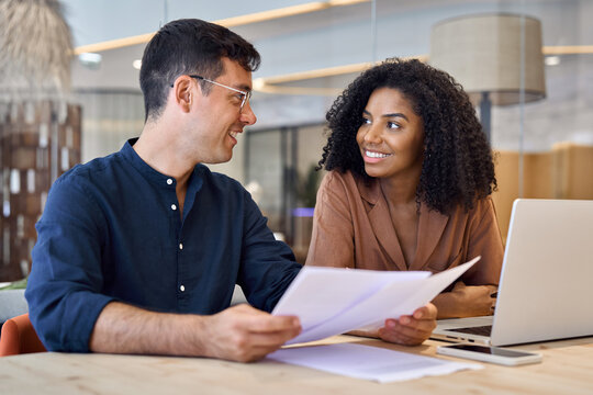 Professional happy busy business team of two diverse employees man and woman, manager and client or colleagues talking using laptop computer discussing documents working in office at work meeting.