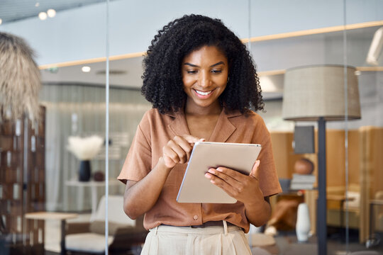 Happy busy young African American professional business woman, female entrepreneur, smiling ethnic lady company employee or executive standing in office using digital tab working on financial project.