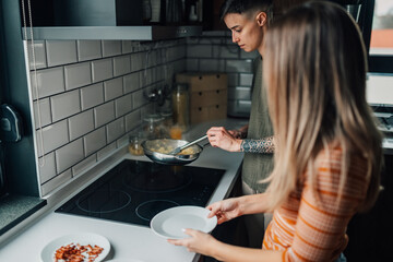 Lesbian couple cooking scrambled eggs together in modern kitchen