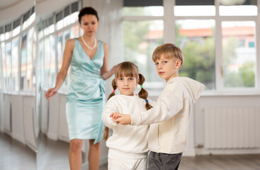 Obraz premium Couple of boy and girl kids dressed in sport wear twirling while taking hustle dancing lessons.
