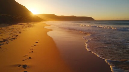A sandy beach at sunrise with smooth, golden sand and cool ocean waves.