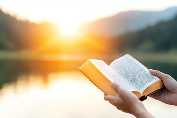 Person holding an open book by a tranquil lake during sunset, surrounded by nature. The serene atmosphere evokes feelings of peace and reflection.