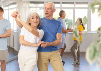 Group of elderly pensioners learn to dance a couple tango dance in a dance class