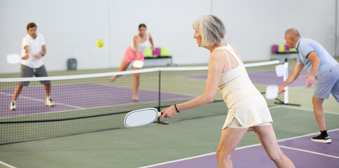 Sportive slim woman with racquet playing pickleball in court. View from the back