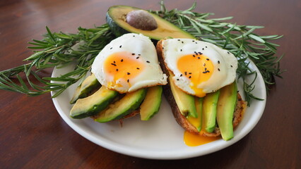 Nutrien Two Toasts avocado and fried egg, rosemary. Preparing healthy avocado toast for breakfast with avocado slices rye wholegrain bread sunny side up egg on top. Healthy breakfast for two, couple