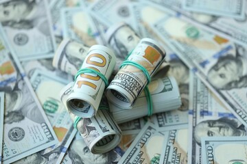 Many rolls of one hundred dollar bills lies on big amount of american currency banknotes