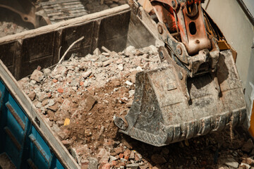 Excavator removing debris from a demolition site and dumping it into the back of a truck