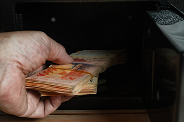 Man taking bundles of cash from inside an open safe.