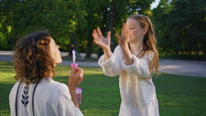 Mother daughter blowing soap bubbles on grass in sunshine park nature closeup