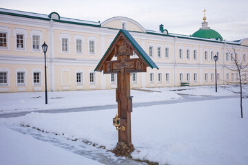 Wooden cross is standing in the snow in front of a large building