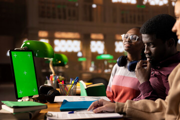 Young student uses mockup display while doing research for exam preparations, reading educational information from reliable academic sources. Pupil completes her notes in the textbook.