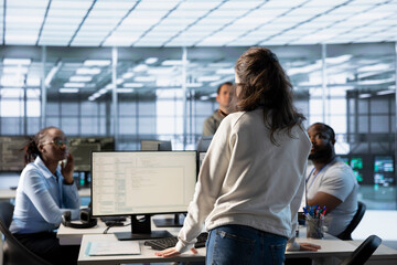 Manager supervising multiethnic team working in data center, raising from desk to make...