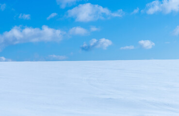 Landscape with a field covered with snow and blue sky with clouds