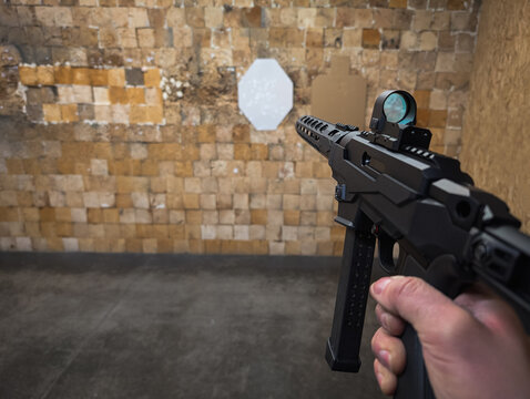 Shooting from a modern 9mm caliber carbine with a holographic sight at a shooting range. Photo from a first-person view.
