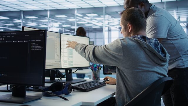 Programmer requesting help from manager while working on computer in data center, monitoring hardware energy consumption. Team leader overseeing IT expert checking for system failures, camera B