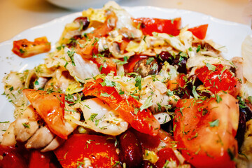 A vibrant plate of tuna salad with fresh tomatoes, beans, herbs, and a mix of colorful vegetables, topped with chopped parsley for a delicious presentation.