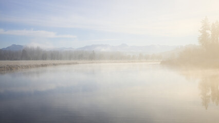 Background warm morning light spreads across foggy blue lake with distant trees and mountains