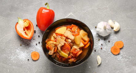 Black bowl with delicious beef stew and different ingredients on grey background