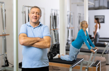 Fototapeta premium Portrait of smiling elderly male pensioner in activewear posing in modern Pilates fitness studio