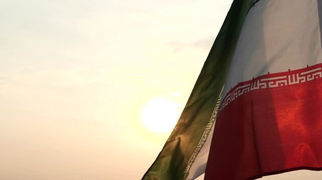 Close up Iran flag waving in the wind against sunset, beautiful cloud sky, outdoor background. Concept of Iran national flag, Iranian, Islamic Republic of Iran, Emblem, Persian, Iranian, War, Freedom