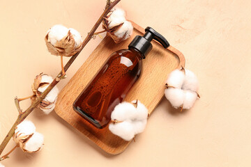 Wooden board with bottle of cosmetic product and cotton branch on color background