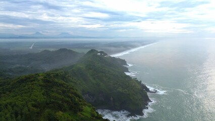 Aerial drone view of coastline with hills and trees, as well as view of coral cliffs and sea with waves from the ocean in Sagara view also known as Karang Bolong Beach Kebumen Central Java Indonesia
