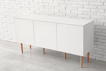 Stylish white chest of drawers near light brick wall in room