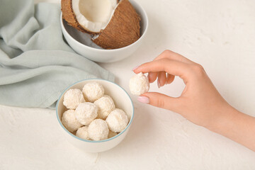 Woman taking tasty coconut candy from bowl on white table
