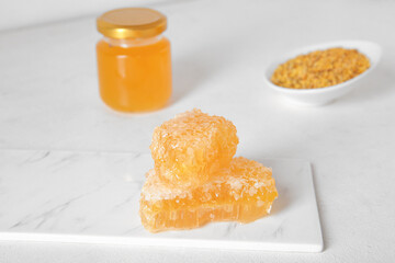 Board with sweet honeycombs and bee pollen on light background