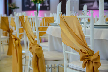 White formal chairs decorated with light brown wedding material