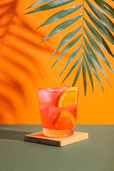 Glass of delicious Negroni cocktail and palm leaf on color background